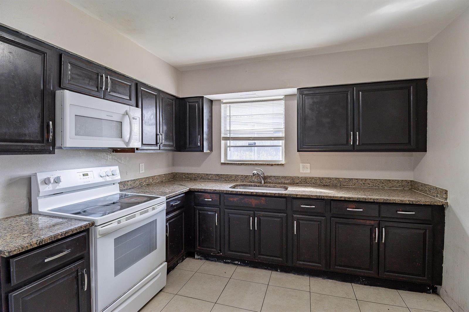A kitchen features dark wood cabinets, granite countertops, white appliances, and light-colored floor tiles — 404 NW 5th Avenue, Boynton Beach FL 33435, BOYNTON BEACH, FL