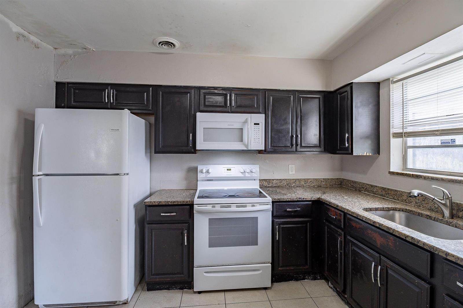 A kitchen features dark wood cabinets, granite countertops, white appliances, and a stainless steel sink — 404 NW 5th Avenue, Boynton Beach FL 33435, BOYNTON BEACH, FL