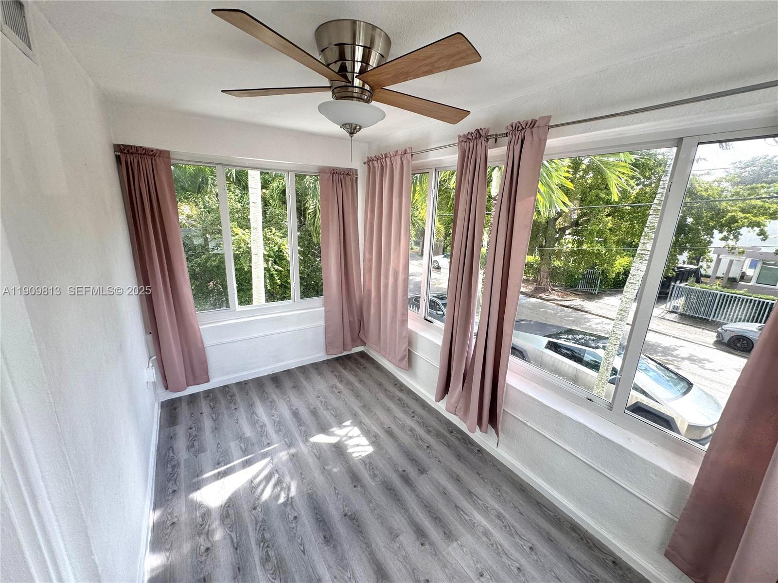 A sunroom features wood-look flooring, a ceiling fan, and large windows with pink curtains — 555 NE 70th St, Miami FL 33138, MIAMI, FL