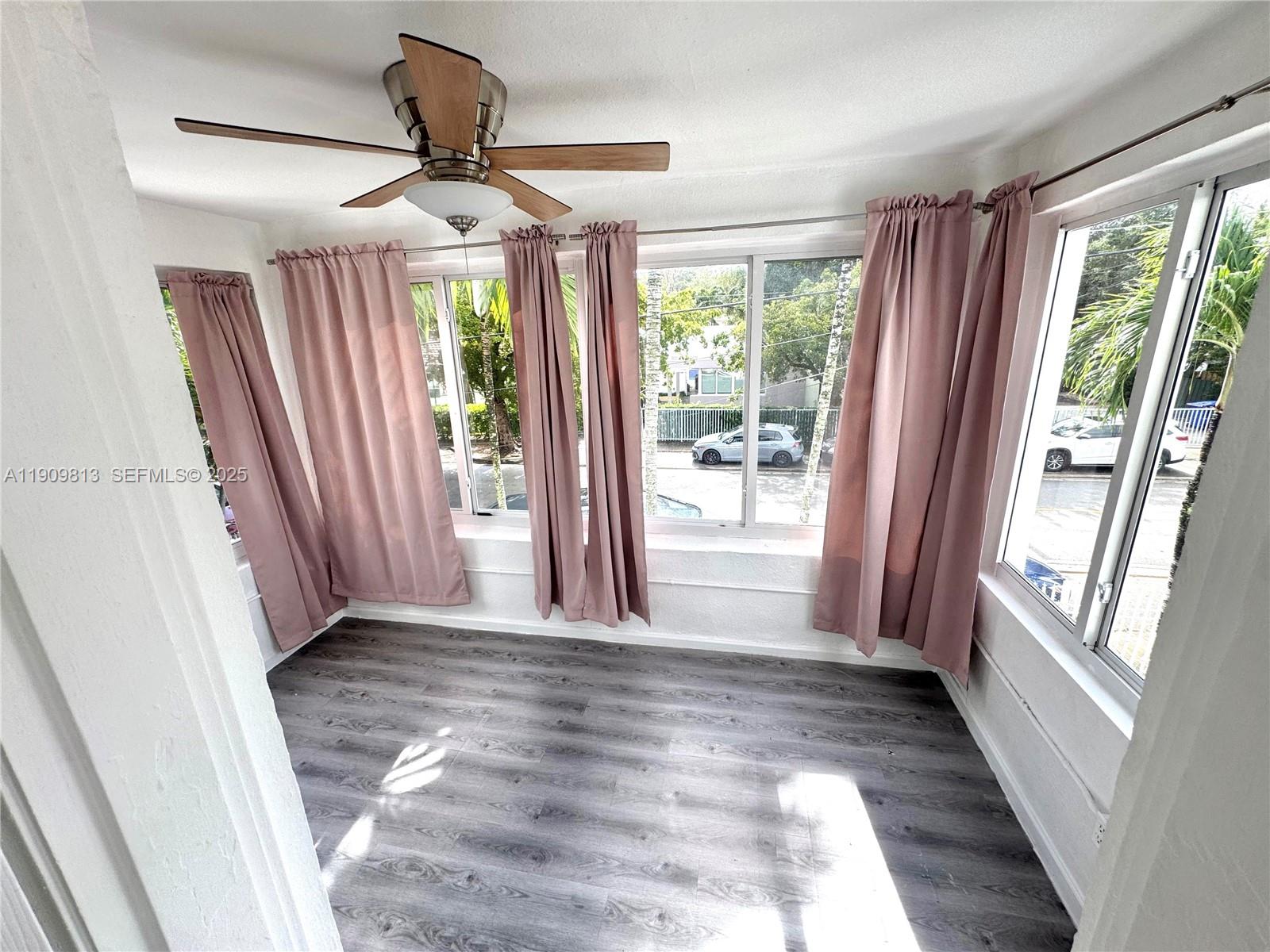 A sunroom with gray wood-look flooring, a ceiling fan, and pink curtains over windows — 555 NE 70th St, Miami FL 33138, MIAMI, FL