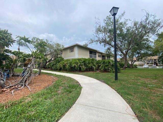 A concrete path leads toward a two-story apartment building surrounded by trees and landscaping — 1656 SUNNY BROOK LANE NE UNIT L102, PALM BAY, FL