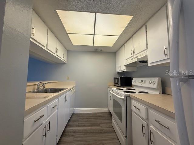 A galley kitchen features white cabinets, light countertops, stainless steel appliances, and wood-look flooring — 1656 SUNNY BROOK LANE NE UNIT L102, PALM BAY, FL