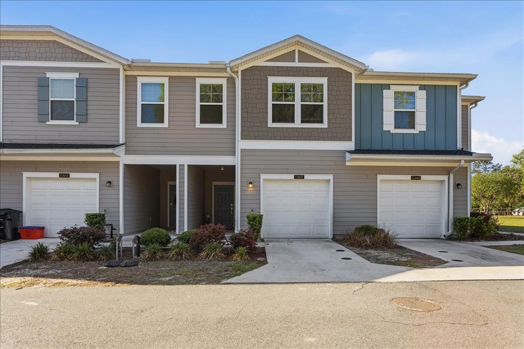A row of three attached townhomes features gray and blue siding with individual white garage doors — 12657 NW 7TH PLACE, NEWBERRY, FL