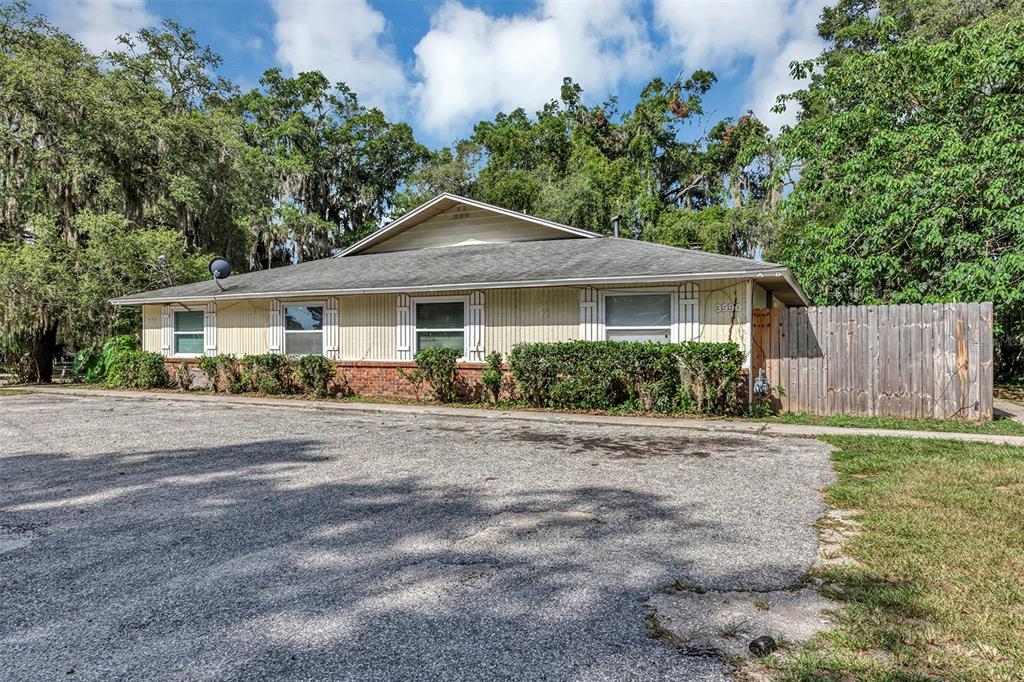 A single-story house with light-colored siding and a brick base sits behind a gravel lot — 3990 SE 17TH COURT, OCALA, FL