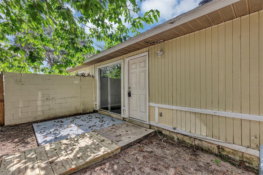 A beige exterior wall features a sliding glass door and a white entry door — 3990 SE 17TH COURT, OCALA, FL