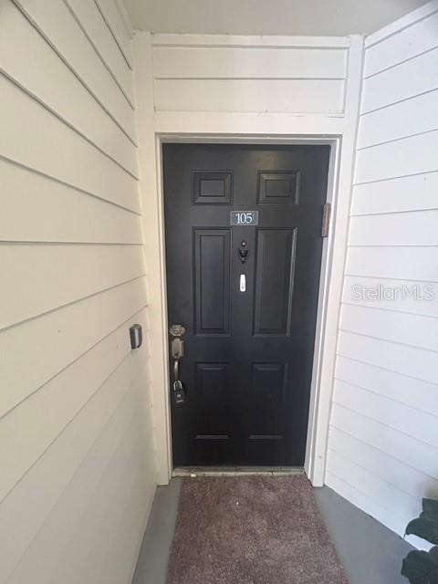 A black front door labeled 105 is set within white horizontal siding — 425 SUMMIT RIDGE PLACE UNIT 105, LONGWOOD, FL