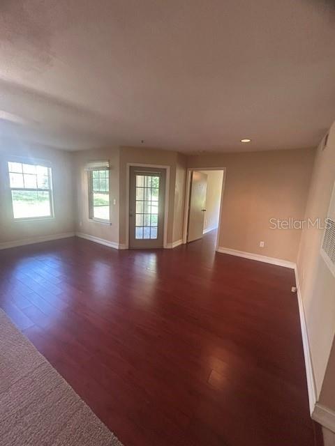 An empty room with dark wood flooring, a glass-paneled door, and windows — 425 SUMMIT RIDGE PLACE UNIT 105, LONGWOOD, FL