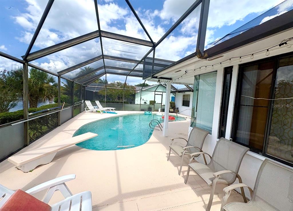 A screened-in patio features a swimming pool with a diving board and outdoor seating — 13 FLARESTONE COURT, PALM COAST, FL
