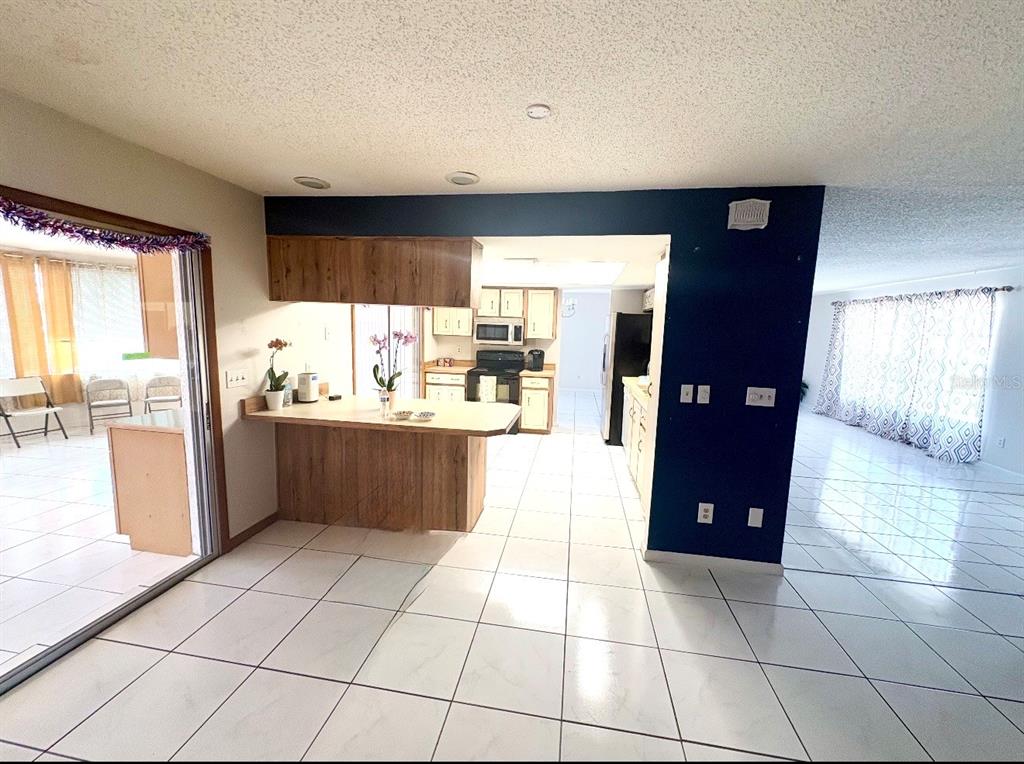 A kitchen with wood cabinets and a breakfast bar opens into a tiled living area — 13 FLARESTONE COURT, PALM COAST, FL