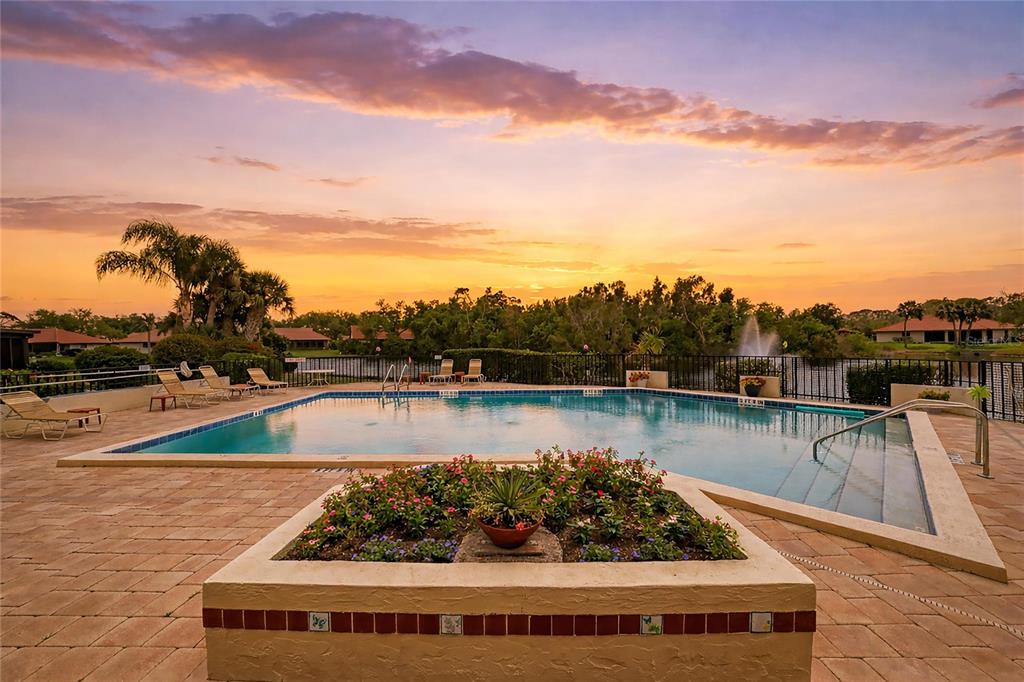 A swimming pool with a stone deck and a central planter at sunset — 246 LAUREL HOLLOW DRIVE UNIT 23, NOKOMIS, FL
