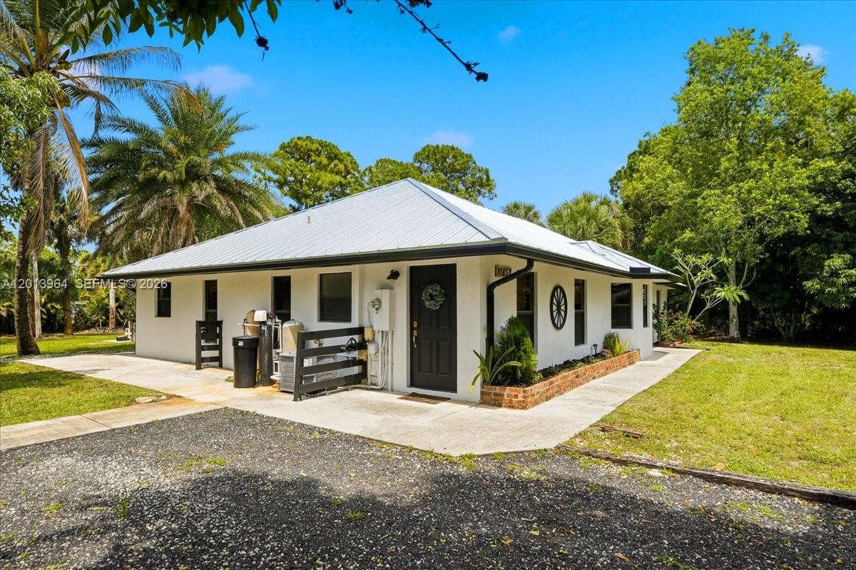 A white single-story house with a metal roof sits on a gravel driveway — 17857 82nd Rd N, Loxahatchee FL 33470, LOXAHATCHEE, FL
