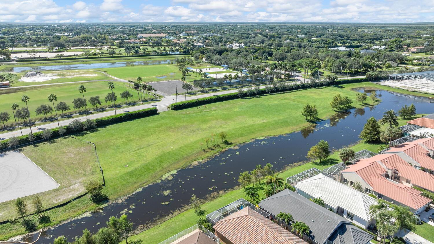 An aerial view shows a residential neighborhood with a canal, green lawns, and palm trees — 2970 Greenbriar Boulevard, Wellington FL 33414, WELLINGTON, FL