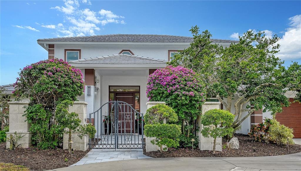 A two-story house features a gated courtyard entrance with lush landscaping and a paved driveway — 7689 COVE TERRACE, SARASOTA, FL