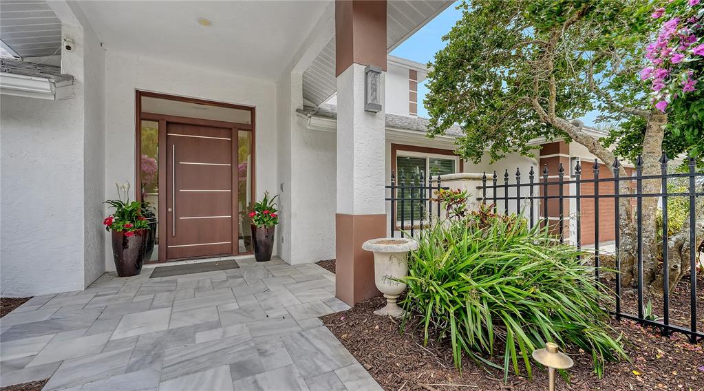 A modern front entrance features a wood door, stone tile porch, and a black metal fence — 7689 COVE TERRACE, SARASOTA, FL