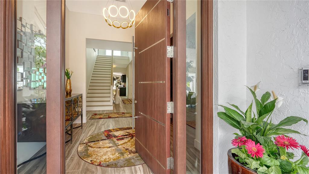 A modern wooden front door opens into a bright foyer with a staircase and chandelier — 7689 COVE TERRACE, SARASOTA, FL