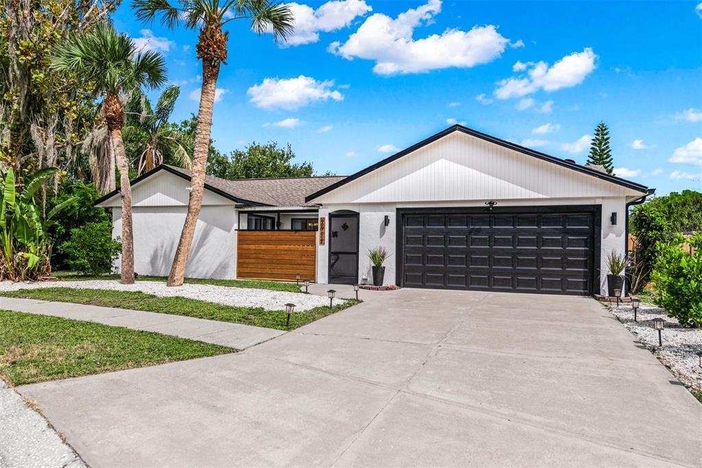 A single-story house with a white exterior, black garage door, and a wood-slatted privacy screen — 2911 WOODPINE COURT, SARASOTA, FL