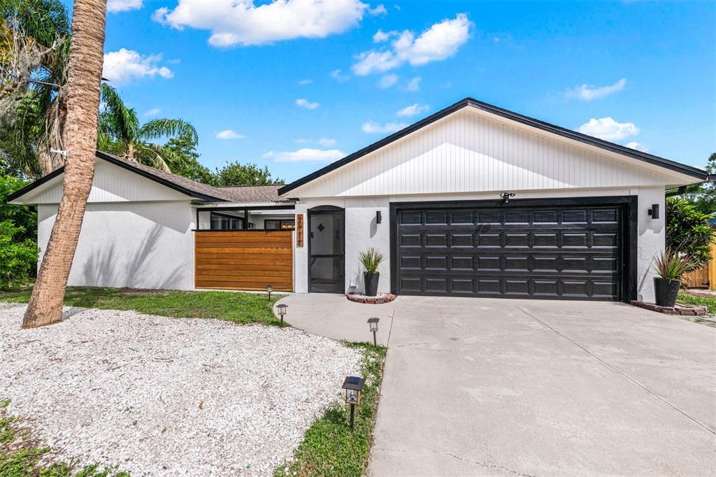 A single-story house with white siding, a black garage door, and a wooden privacy screen — 2911 WOODPINE COURT, SARASOTA, FL