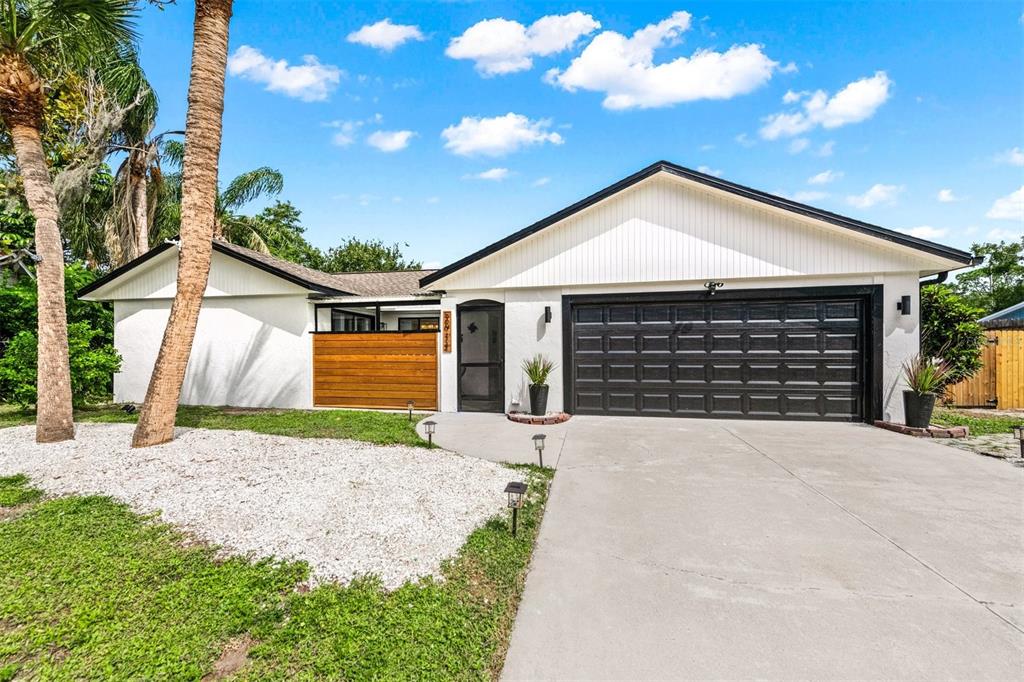 A single-story house features a white exterior, a black garage door, and a wooden privacy screen — 2911 WOODPINE COURT, SARASOTA, FL