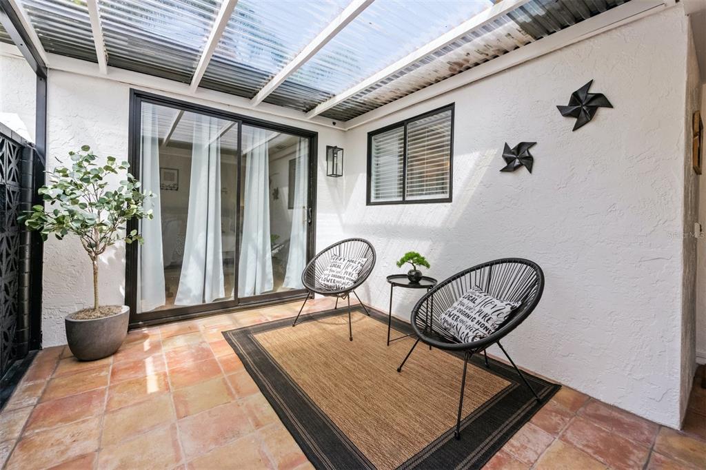 A covered patio features terracotta tile flooring, two black chairs, and a small side table — 2911 WOODPINE COURT, SARASOTA, FL