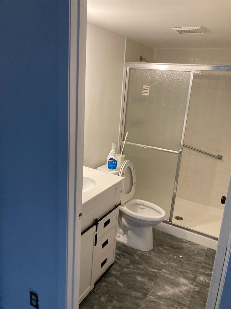 A bathroom features a white vanity, a toilet, and a glass-enclosed shower with gray flooring — WEST PALM BEACH, FL