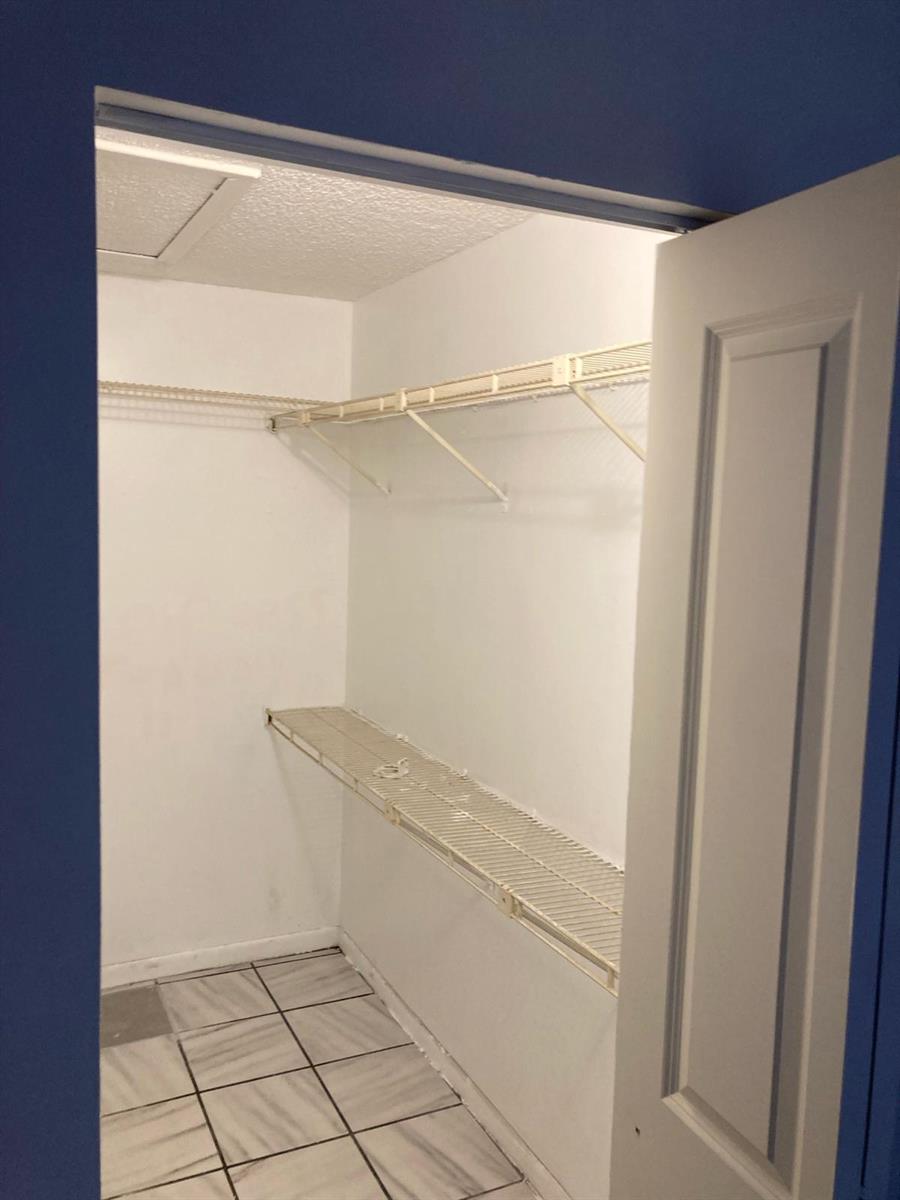 A walk-in closet with white wire shelving, white walls, and light-colored tile flooring — WEST PALM BEACH, FL