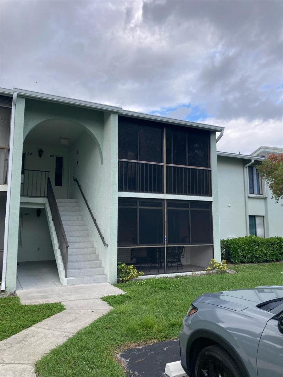 A two-story apartment building features a screened-in balcony and patio with an exterior staircase — WEST PALM BEACH, FL