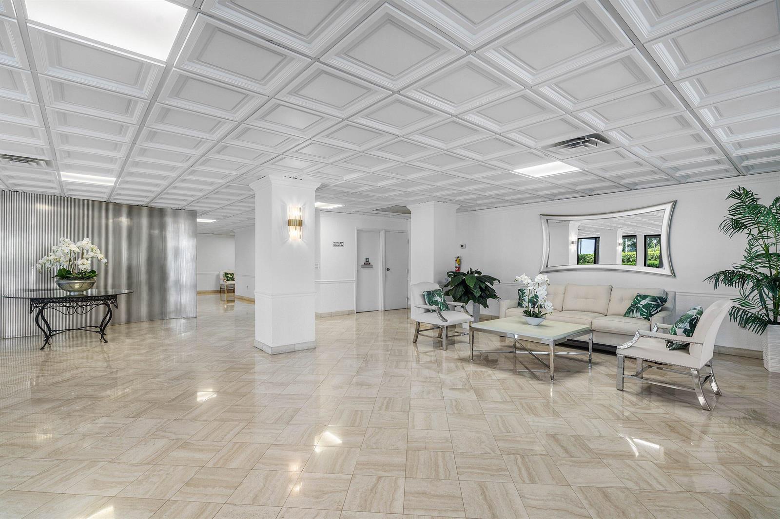 A bright lobby features a coffered ceiling, tiled floors, a white sofa, and a large mirror — 3460 S Ocean Boulevard # 1080, Palm Beach FL 33480, PALM BEACH, FL