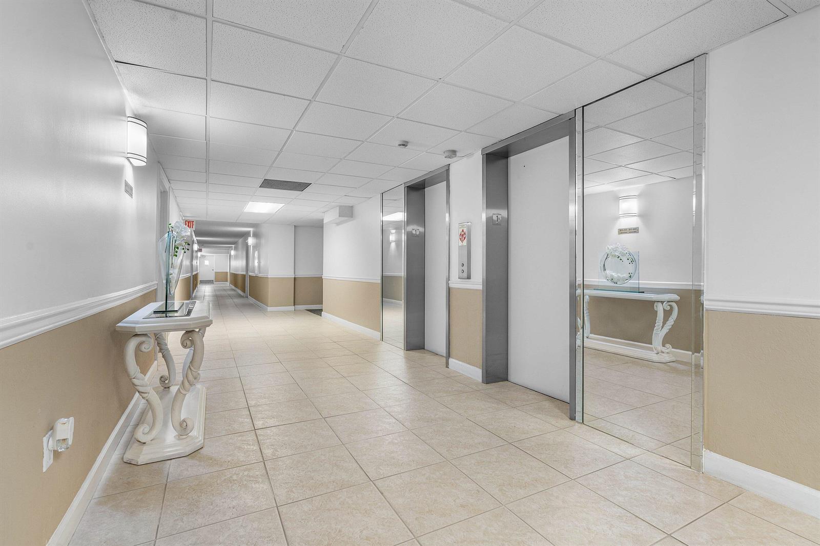 A brightly lit hallway features tiled floors, beige wainscoting, and two elevator doors — 3460 S Ocean Boulevard # 1080, Palm Beach FL 33480, PALM BEACH, FL