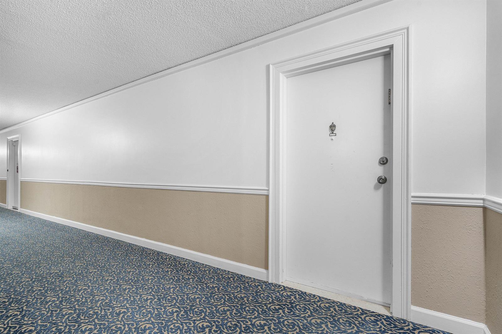 A long apartment hallway features patterned blue carpet, white walls, and a beige wainscot — 3460 S Ocean Boulevard # 1080, Palm Beach FL 33480, PALM BEACH, FL