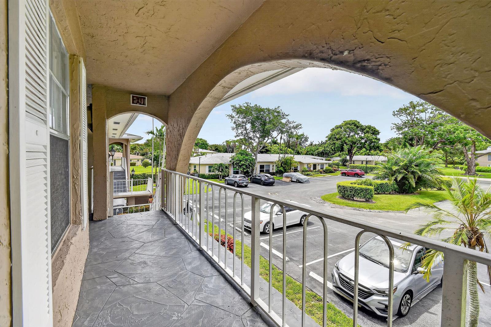 A covered balcony with a stone-patterned floor overlooks a parking lot and residential buildings — 13837 Via Flora, Delray Beach FL 33484, DELRAY BEACH, FL