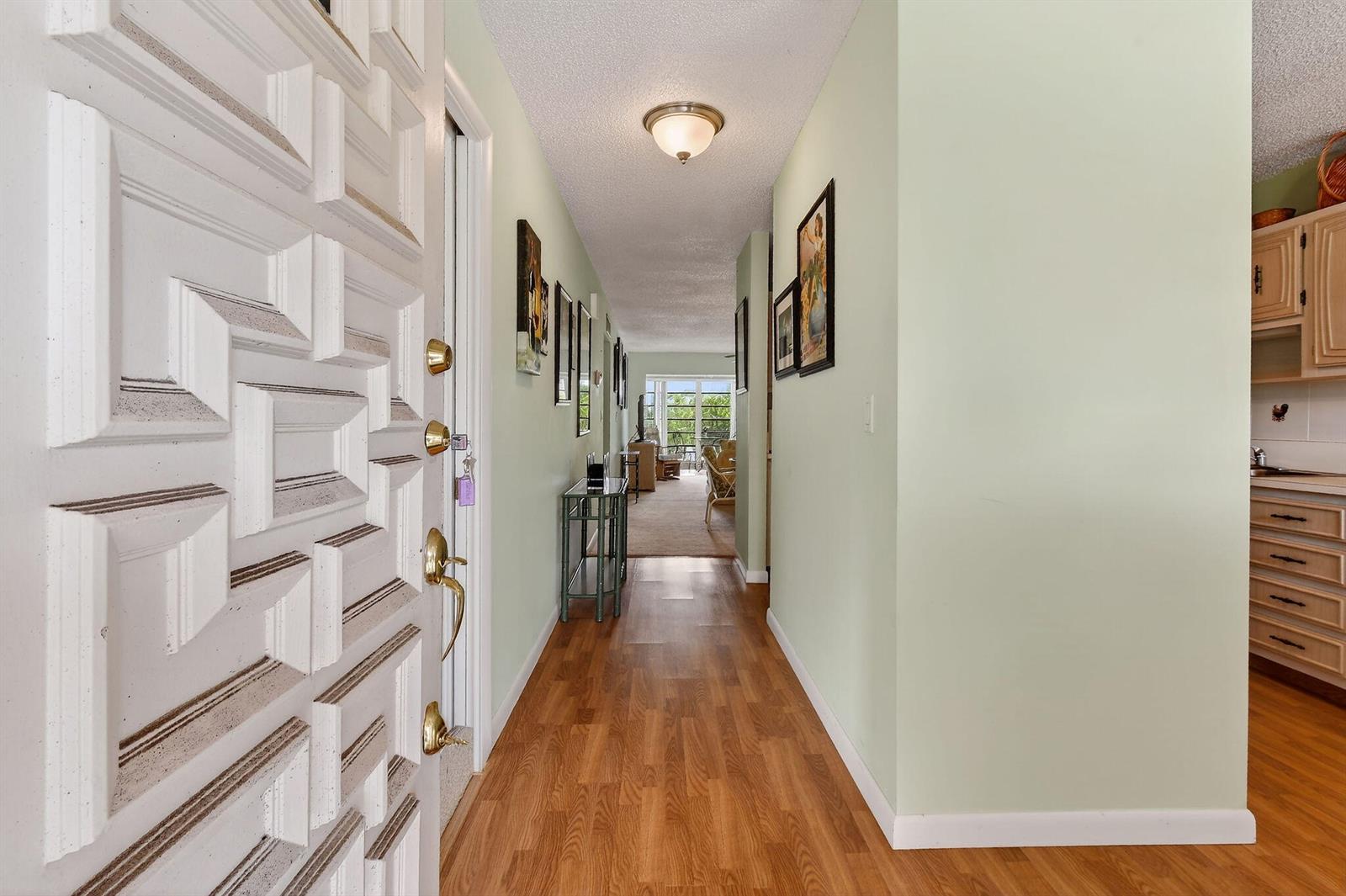 A view from an open front door into a hallway with light green walls and wood-look flooring — 13837 Via Flora, Delray Beach FL 33484, DELRAY BEACH, FL