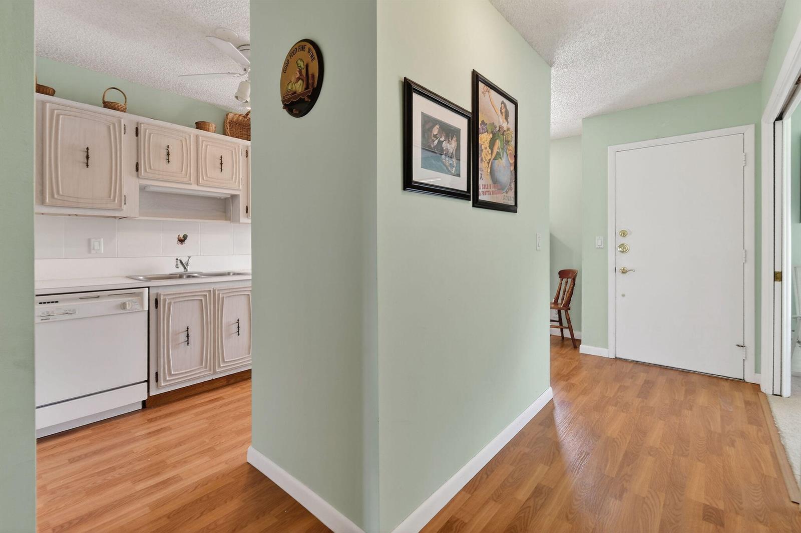 A kitchen with white cabinets and a dishwasher sits beside a hallway with light-green walls — 13837 Via Flora, Delray Beach FL 33484, DELRAY BEACH, FL