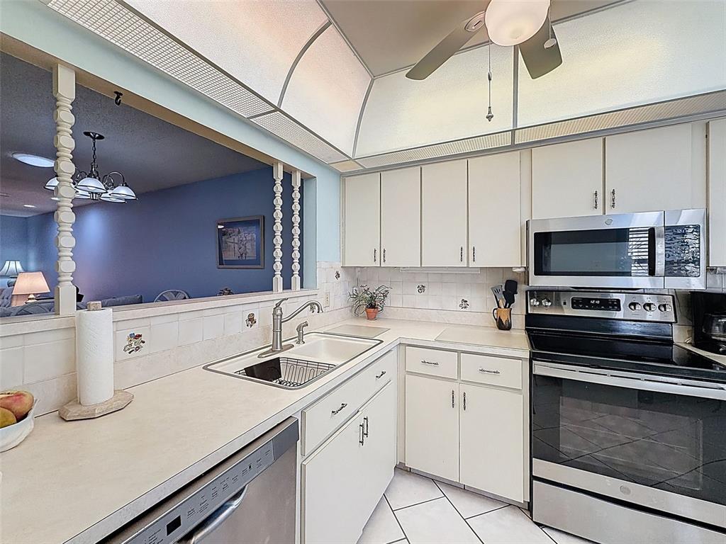 A kitchen features white cabinets, stainless steel appliances, tile countertops, and a pass-through window — 11241 VERSAILLES LANE UNIT 0, PORT RICHEY, FL