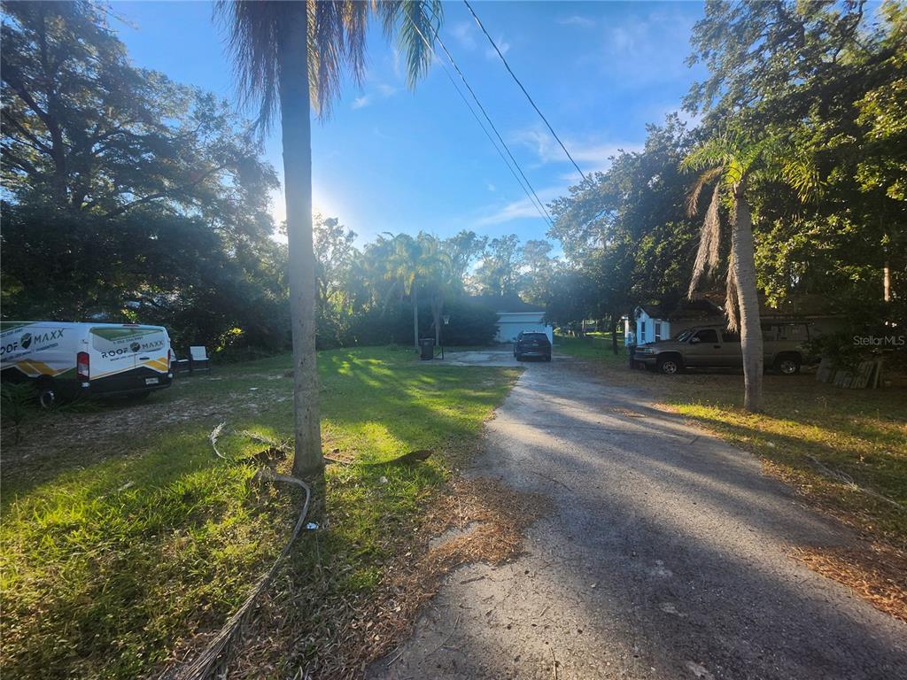 A gravel driveway leads toward a house surrounded by trees and parked vehicles — 7224 N OLA AVENUE, TAMPA, FL