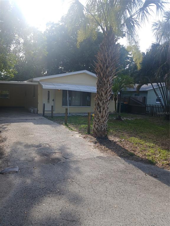 A pale yellow single-story house features a concrete driveway, a carport, and a palm tree — 5410 70TH WAY N, ST PETERSBURG, FL