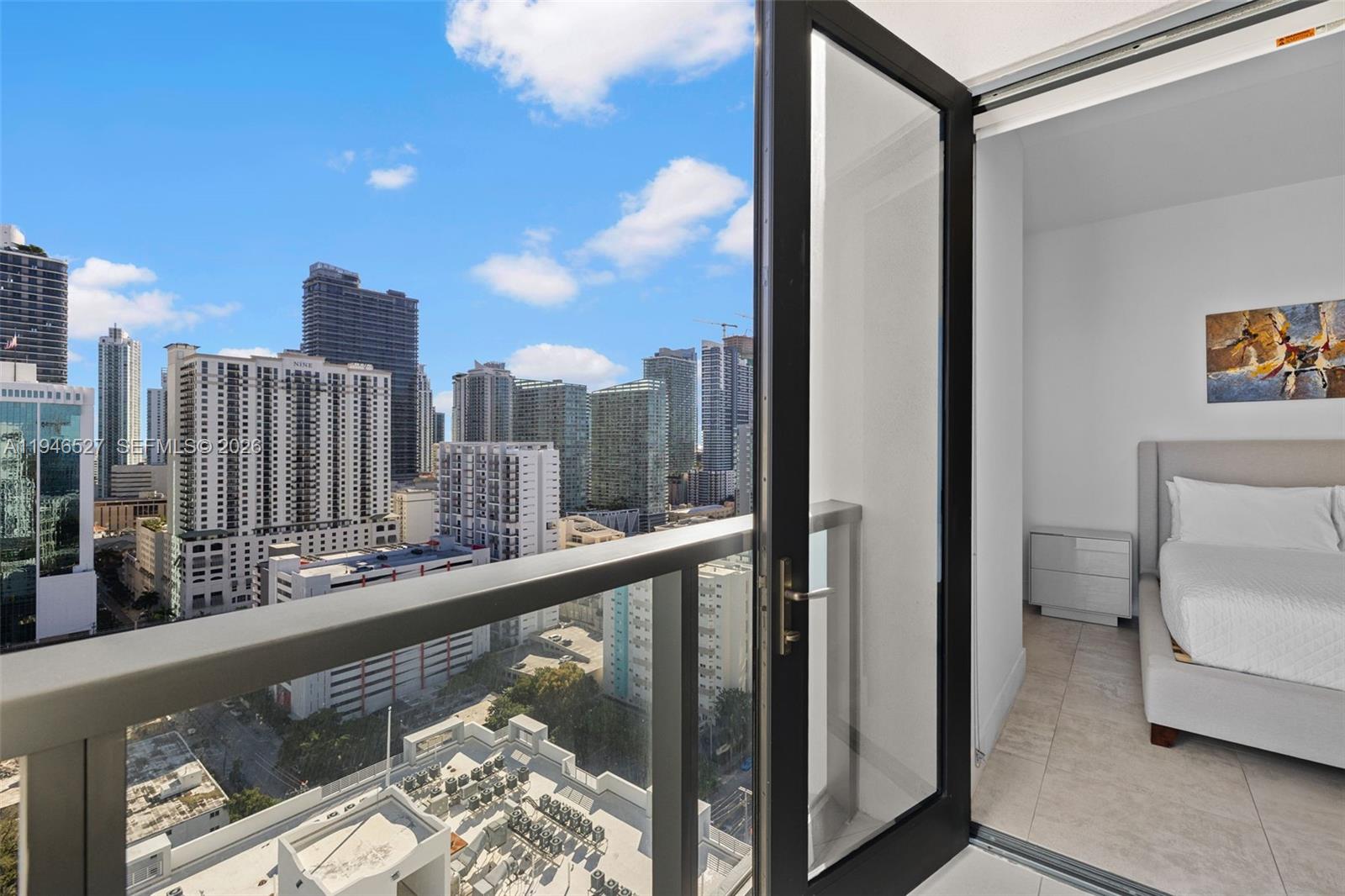 A bedroom with a bed and artwork opens onto a balcony overlooking a city skyline — 239 SW 9th St # 2304, Miami FL 33130, MIAMI, FL