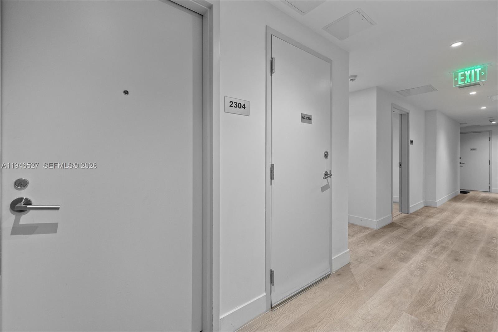 A hallway features white doors, light wood-look flooring, and a green illuminated exit sign — 239 SW 9th St # 2304, Miami FL 33130, MIAMI, FL