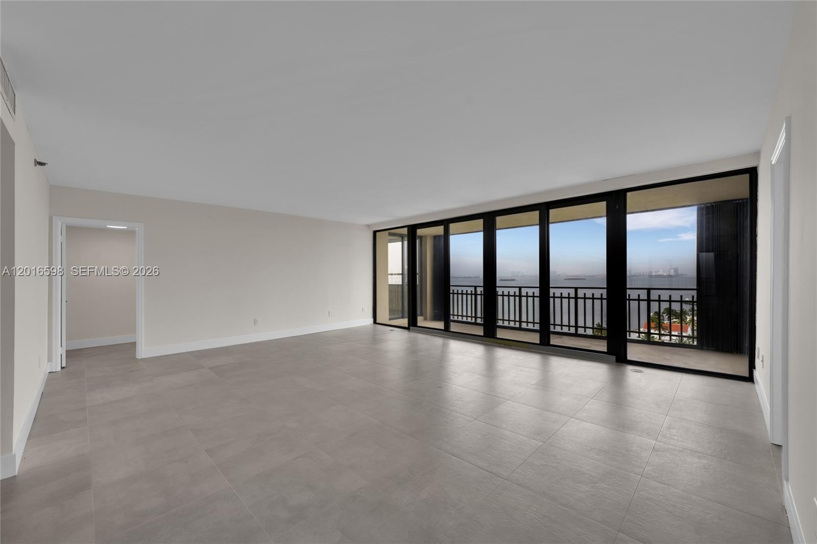 An empty room features large floor-to-ceiling windows, gray tile flooring, and a balcony view — 11113 Biscayne Blvd # 1253, Miami FL 33181, MIAMI, FL