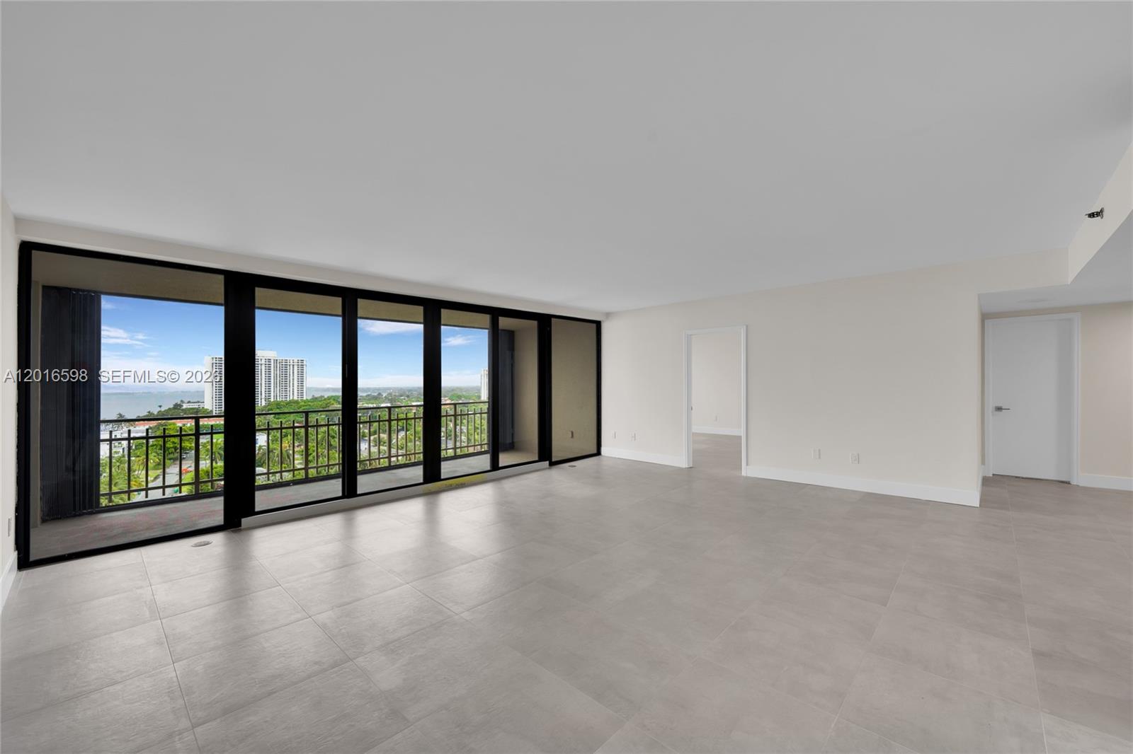 An empty room with large sliding glass doors, a balcony, and light-colored tile flooring — 11113 Biscayne Blvd # 1253, Miami FL 33181, MIAMI, FL