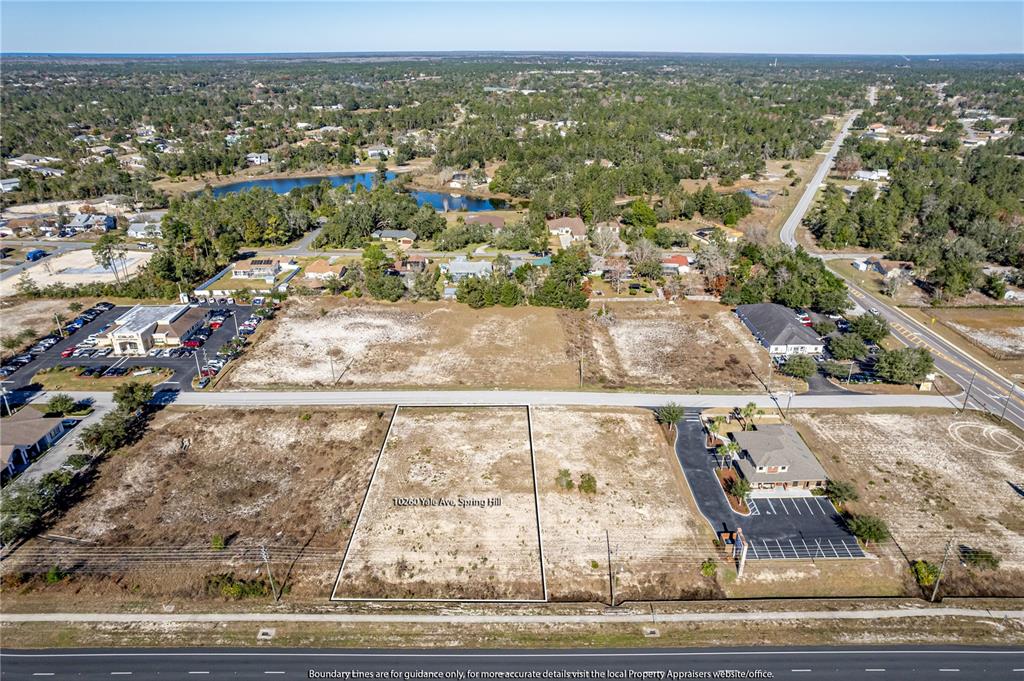 An aerial view shows a vacant rectangular lot outlined in white next to a commercial building — 10260 YALE AVENUE, WEEKI WACHEE, FL
