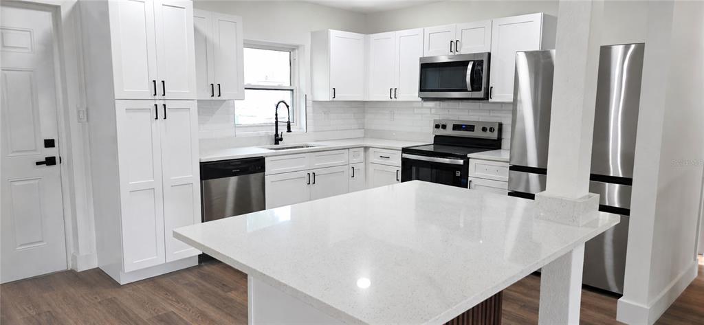 A modern kitchen features white cabinets, stainless steel appliances, and a white quartz island countertop — 180 N KENTUCKY AVENUE, UMATILLA, FL