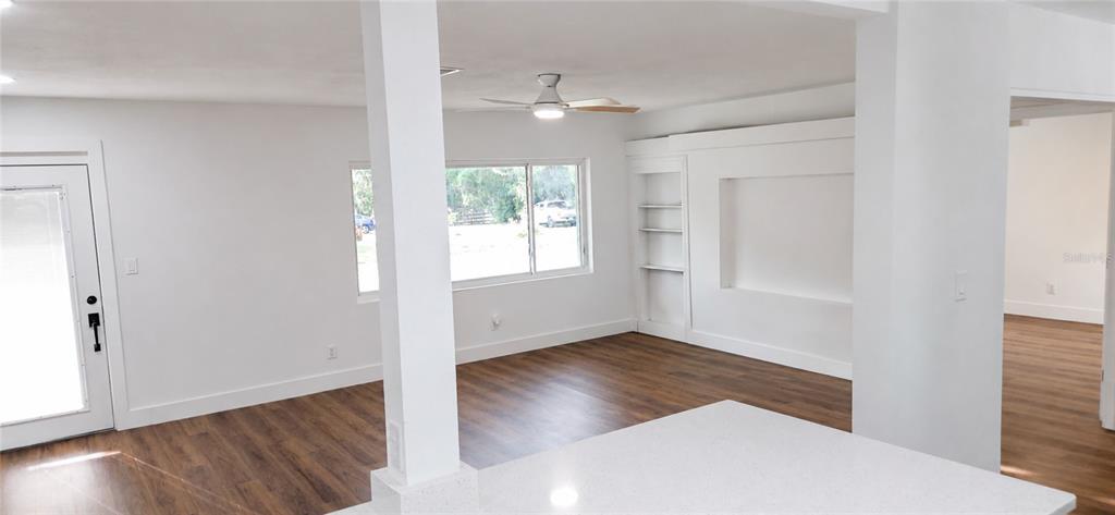 A bright living area features white walls, wood-look flooring, a ceiling fan, and built-in shelving — 180 N KENTUCKY AVENUE, UMATILLA, FL