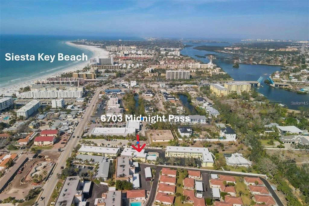 An aerial view shows a multi-story residential complex near a beach and waterway — 6703 MIDNIGHT PASS ROAD UNIT 217, SARASOTA, FL