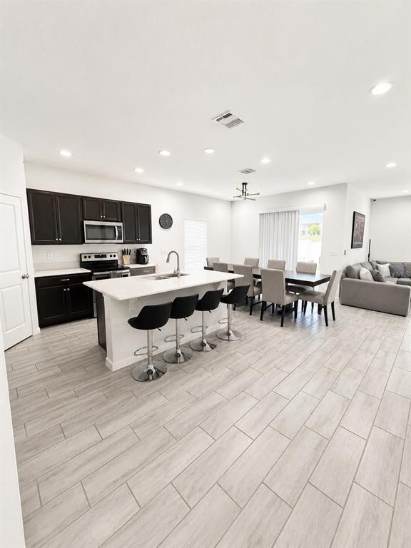 An open-concept kitchen features dark cabinets, a white island with bar seating, and dining area — 124 BELLA VERANO WAY, DAVENPORT, FL