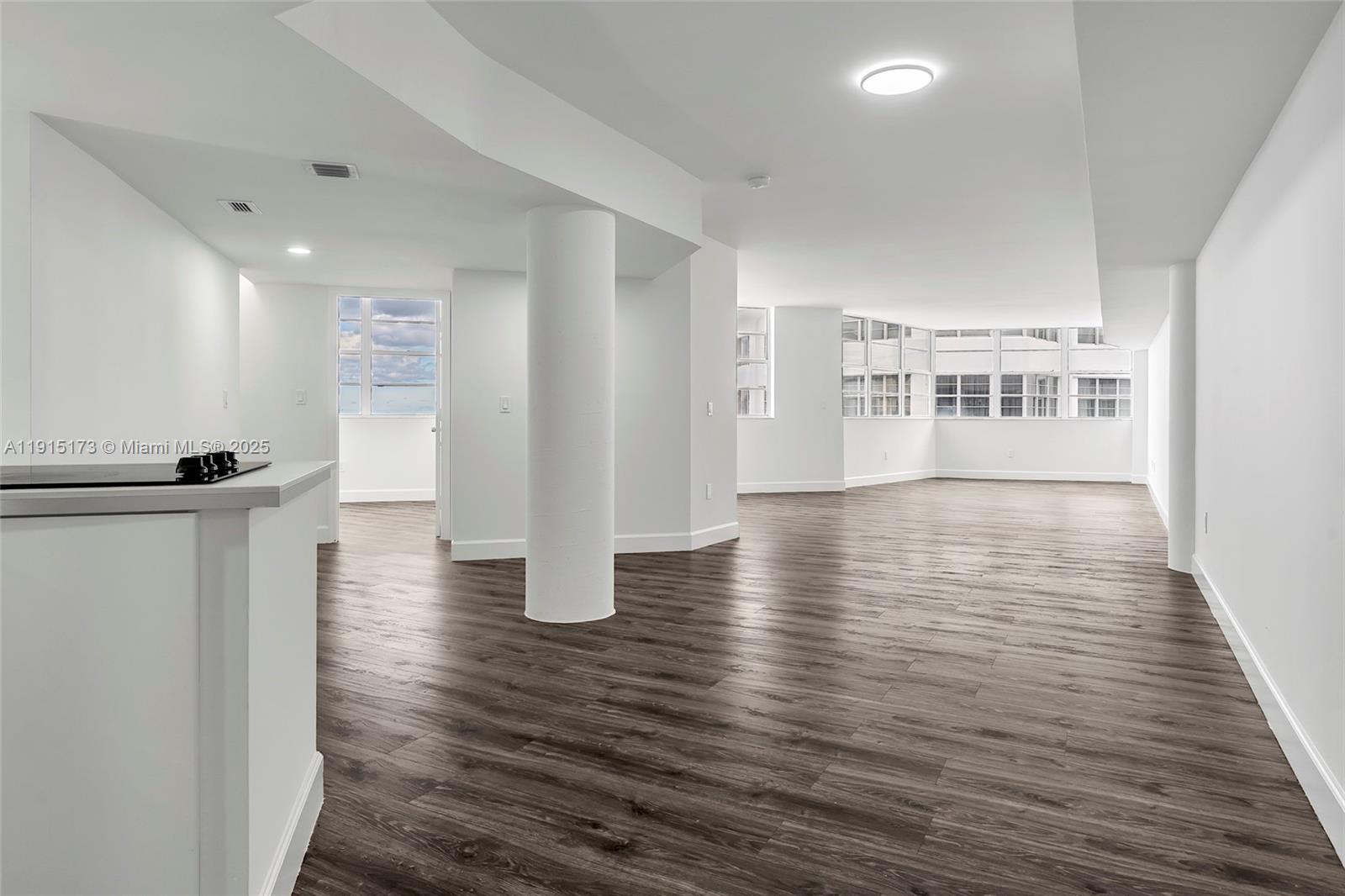 An open-concept living area features white walls, dark wood-look flooring, and a central structural column — 825 Brickell Bay Dr # 1942, Miami FL 33131, MIAMI, FL