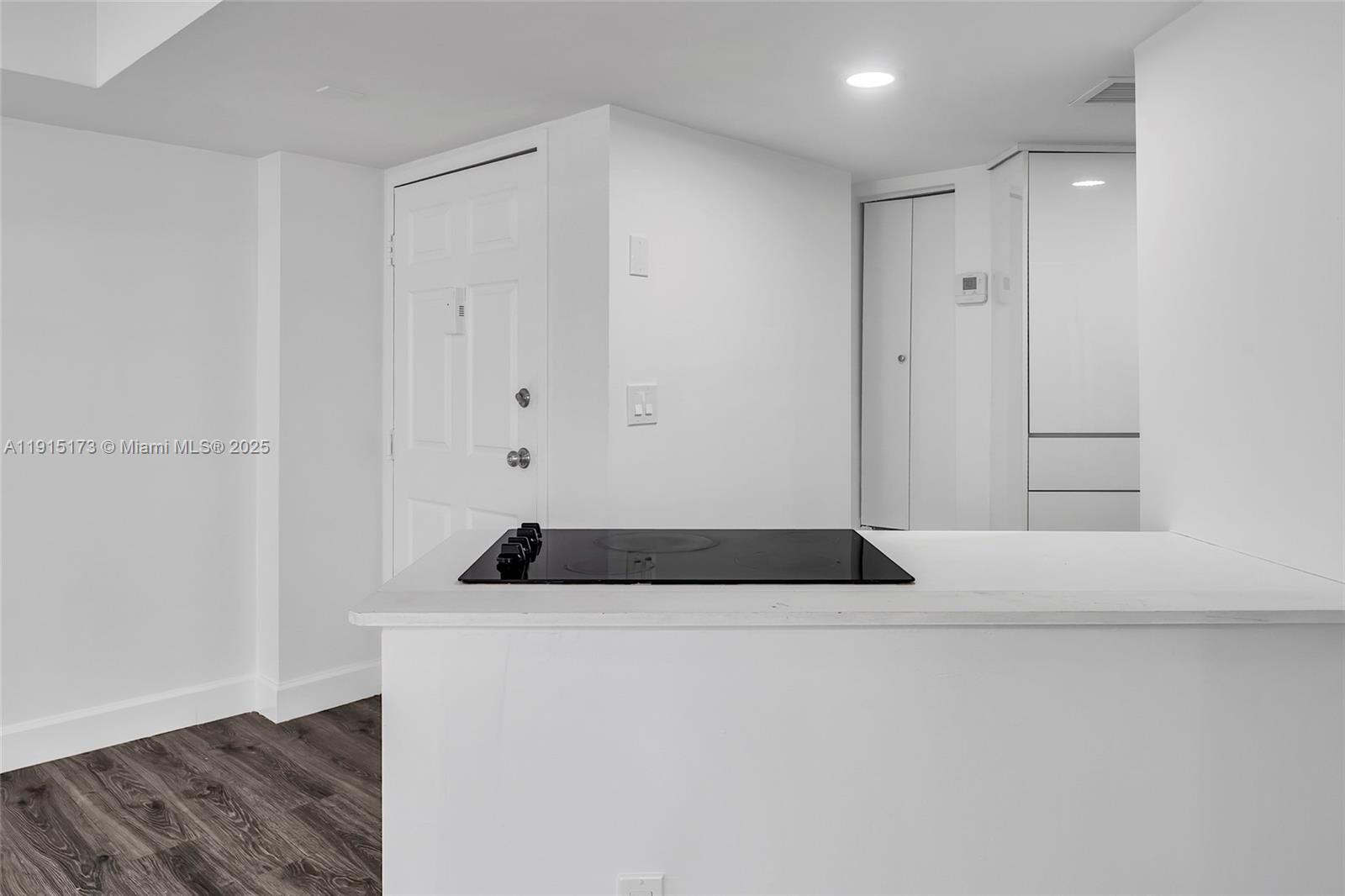 A white kitchen counter features a black electric cooktop in a minimalist room — 825 Brickell Bay Dr # 1942, Miami FL 33131, MIAMI, FL