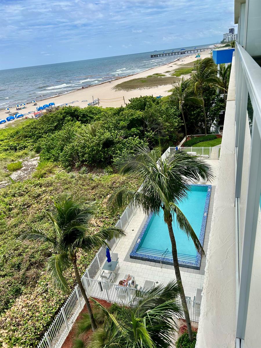 An elevated view shows a swimming pool, palm trees, and a sandy beach with ocean waves — 704 N Ocean Boulevard # 504, Pompano Beach FL 33062, POMPANO BEACH, FL