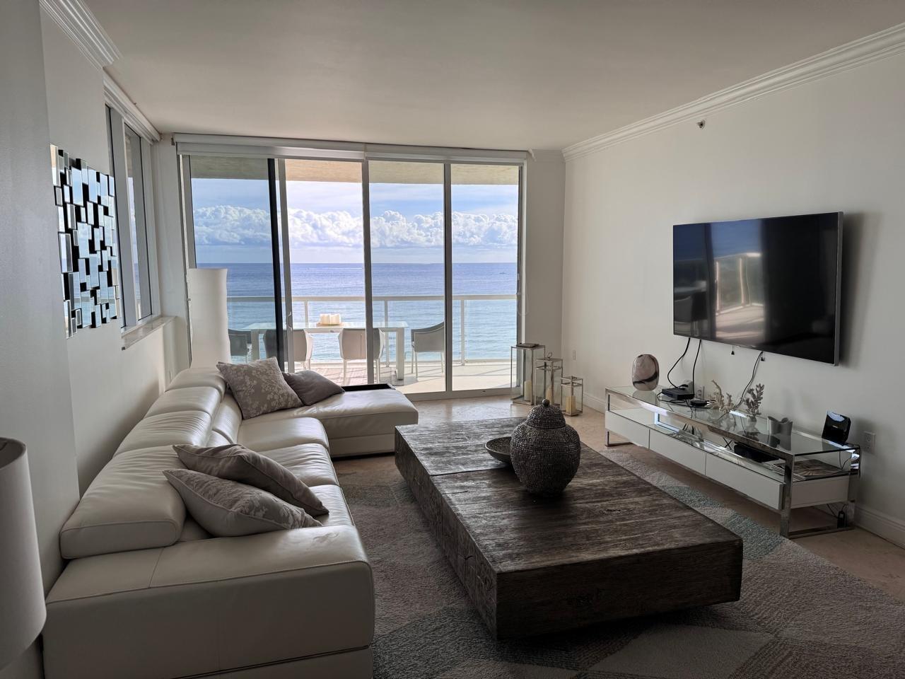 A living room with a white sectional sofa, large wooden coffee table, and ocean view balcony — 704 N Ocean Boulevard # 504, Pompano Beach FL 33062, POMPANO BEACH, FL