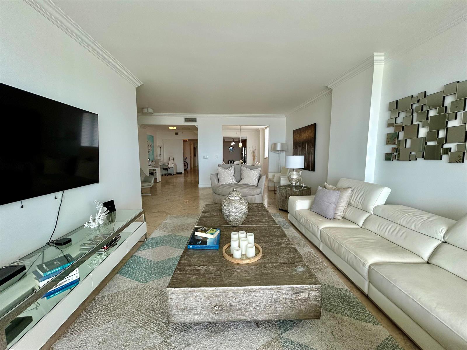 A living room features a white leather sofa, a large wooden coffee table, and television — 704 N Ocean Boulevard # 504, Pompano Beach FL 33062, POMPANO BEACH, FL