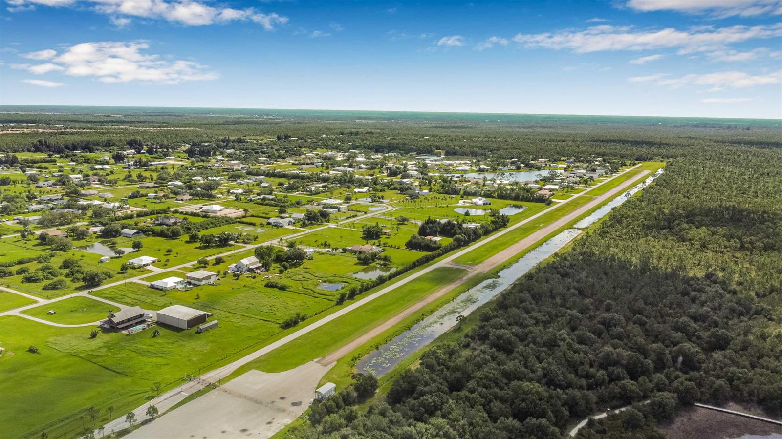 An aerial view shows a residential neighborhood bordering a long airstrip and dense forest — 18742 Crosswind Avenue, FL 33917, FL
